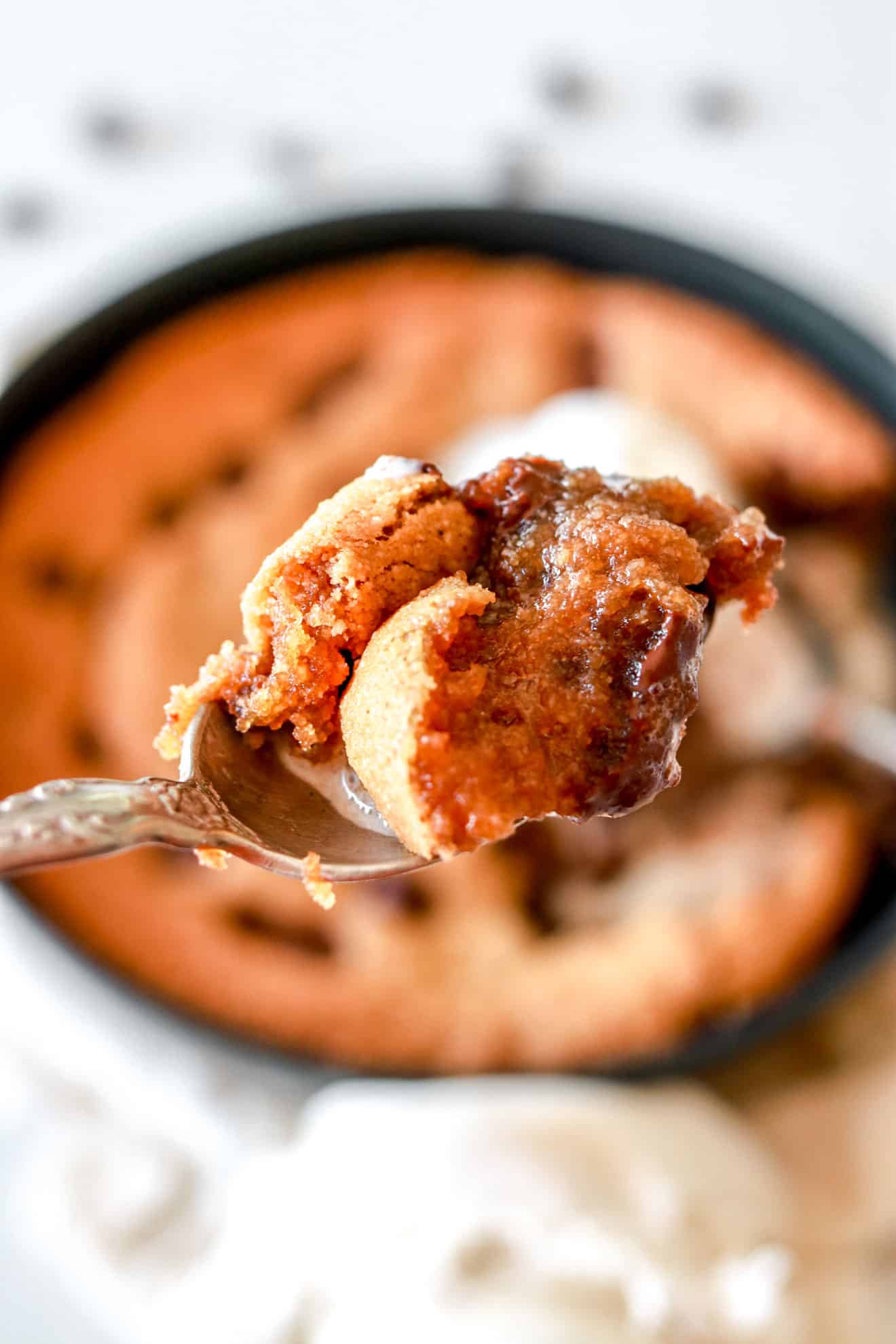 close up of a spoonful of chocolate chip cookie skillet with the cookie skillet blurred in the background