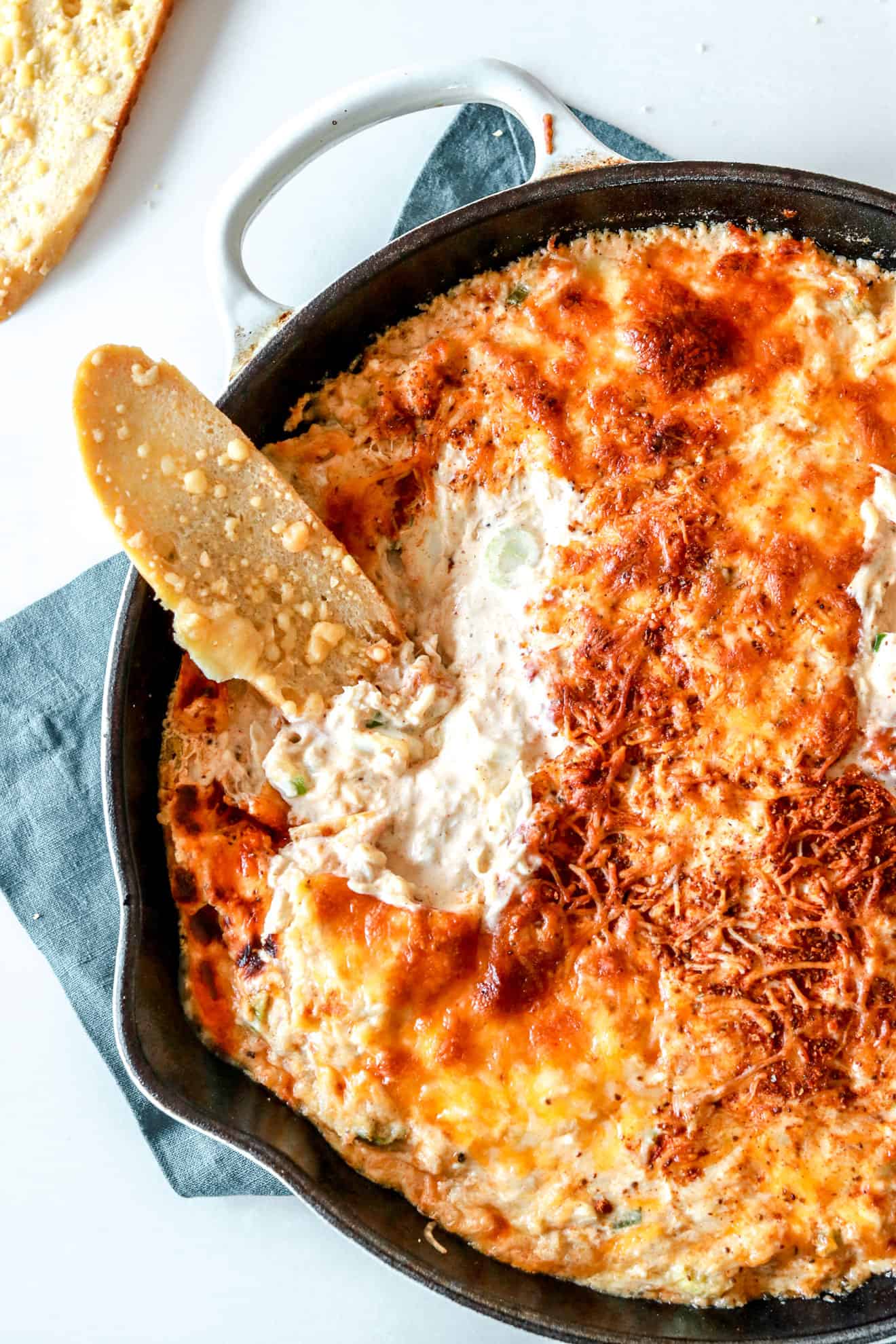 skillet filled with golden brown, hot crab dip with bread dipping into it
