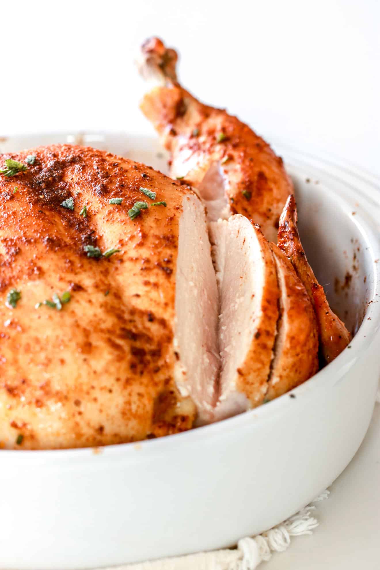 whole roasted chicken in white baking dish with cuts in the breast