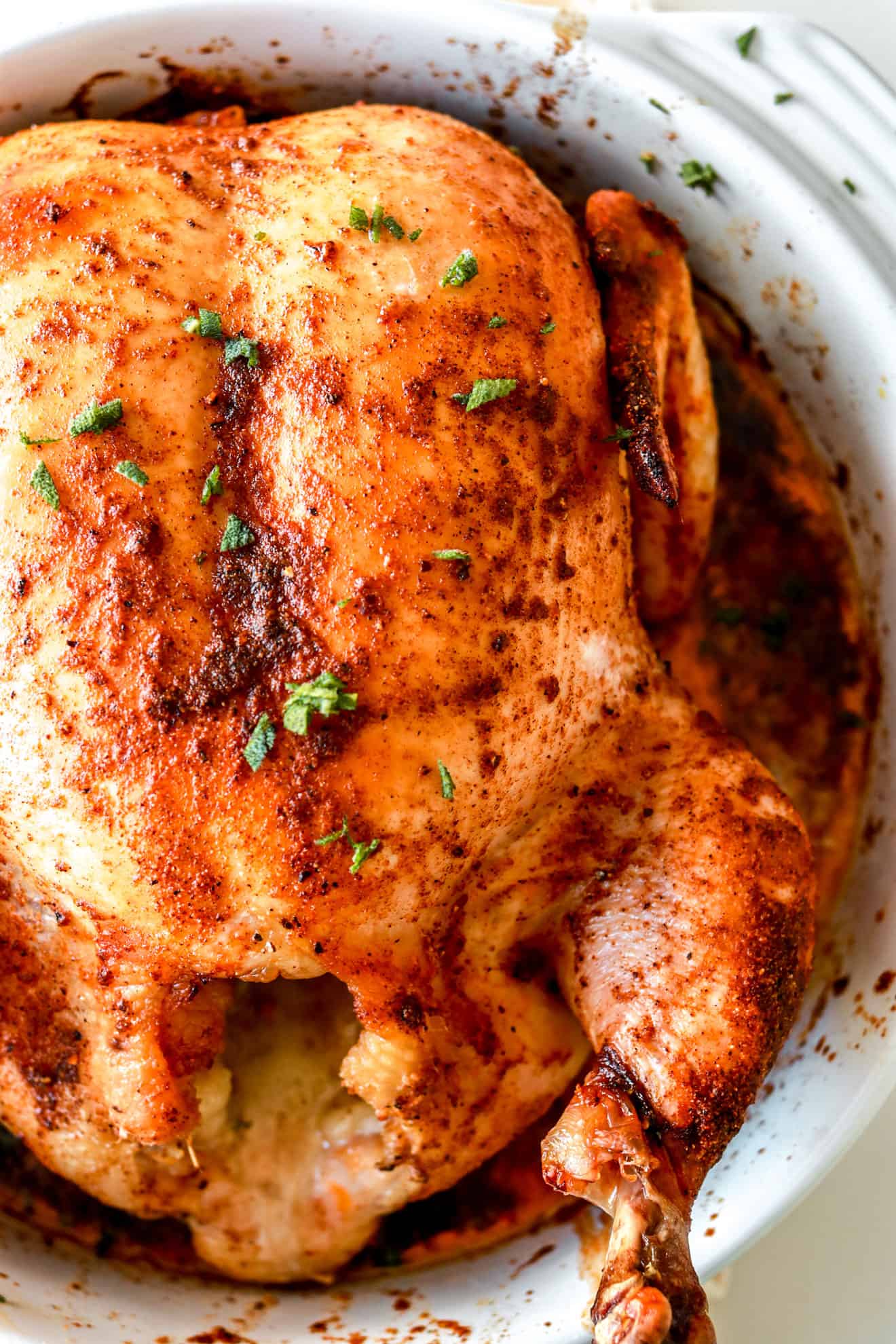close up top down view of a whole roasted chicken in white baking dish