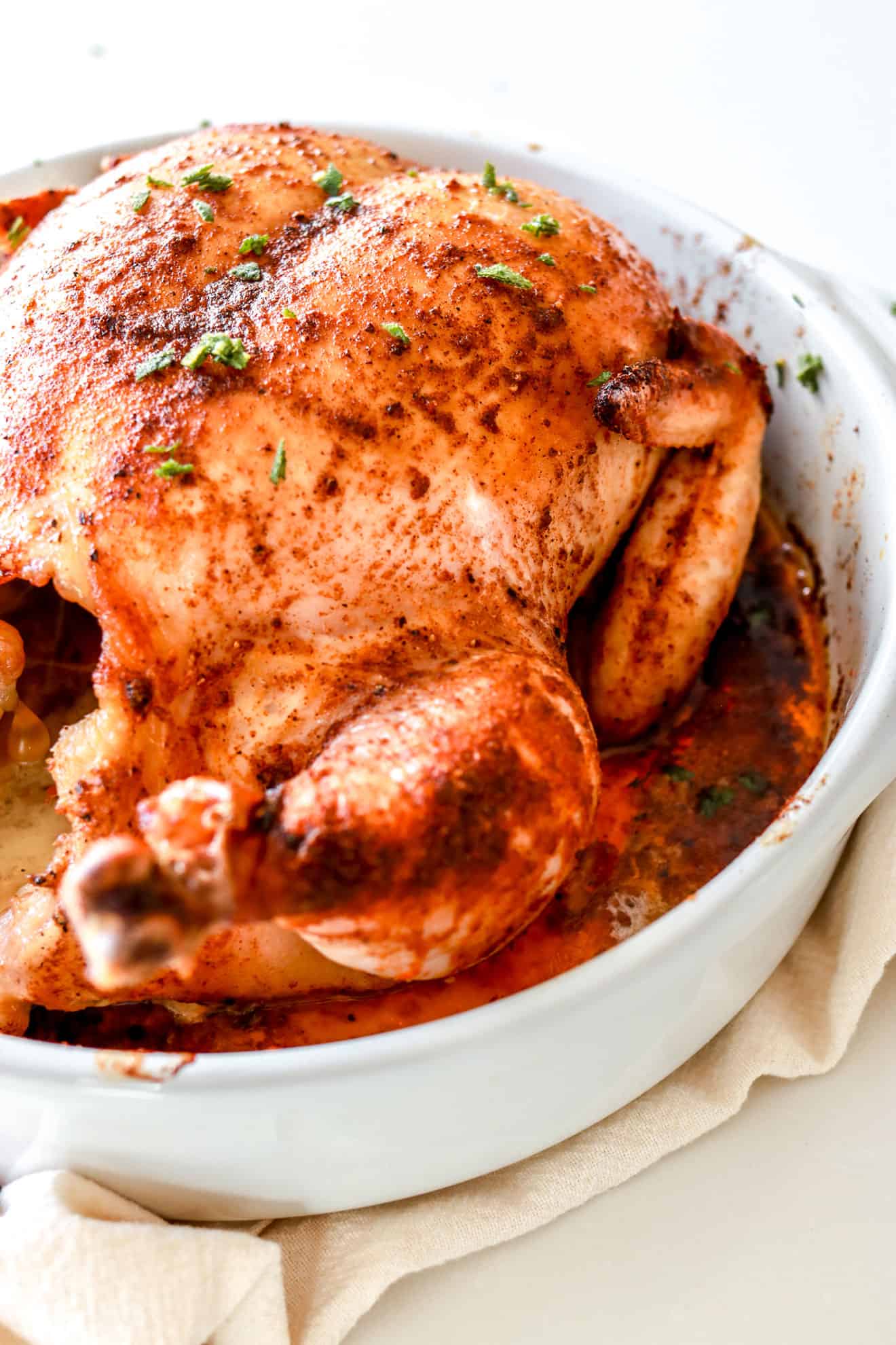 side view of a whole roasted chicken in white baking dish