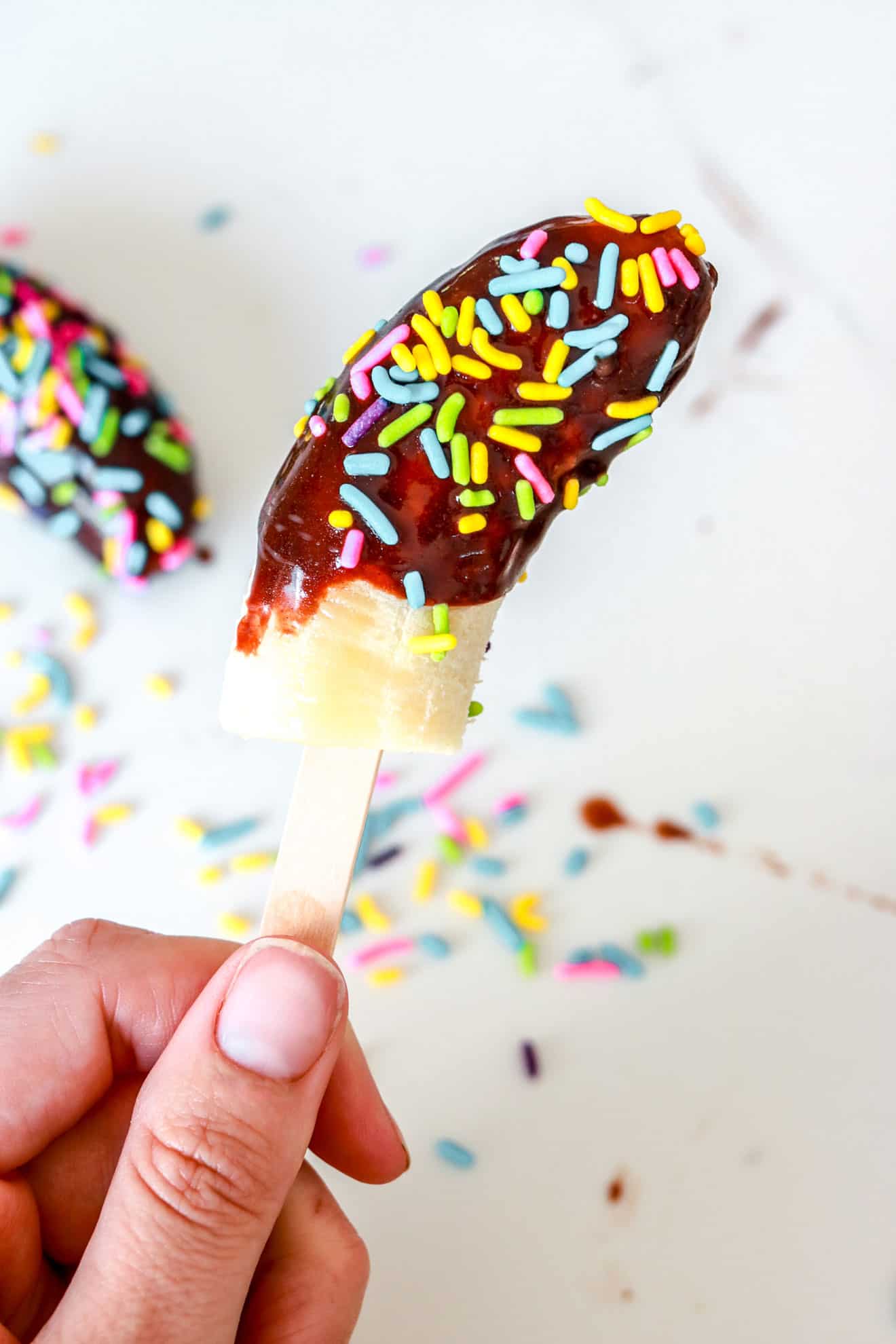 hand holding a Chocolate Covered Banana Pops coated in chocolate with sprinkles
