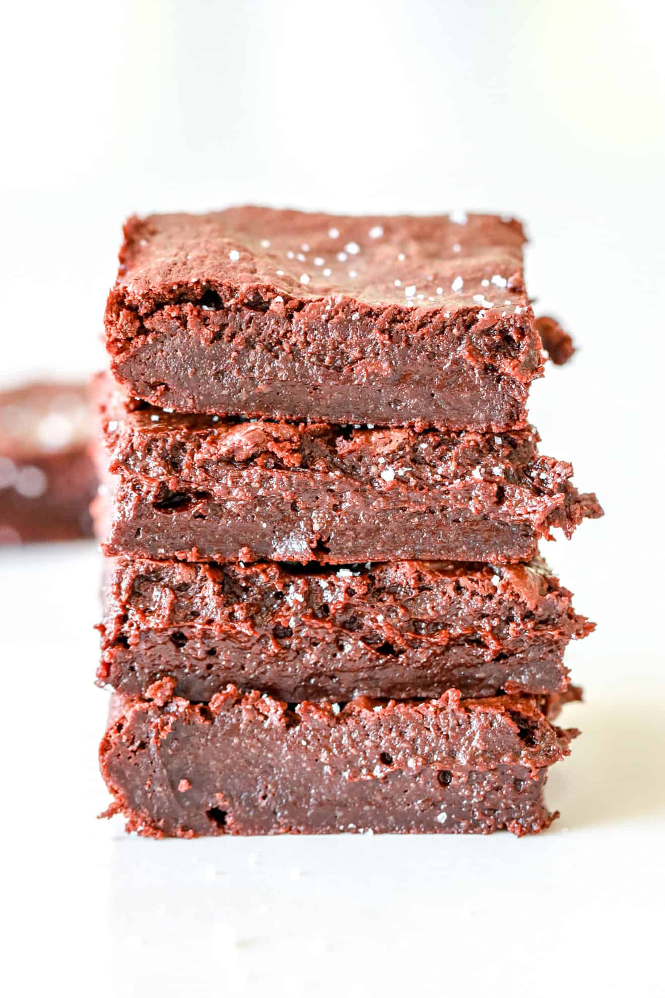 stack of fudgey gluten free brownies on white counter with white background