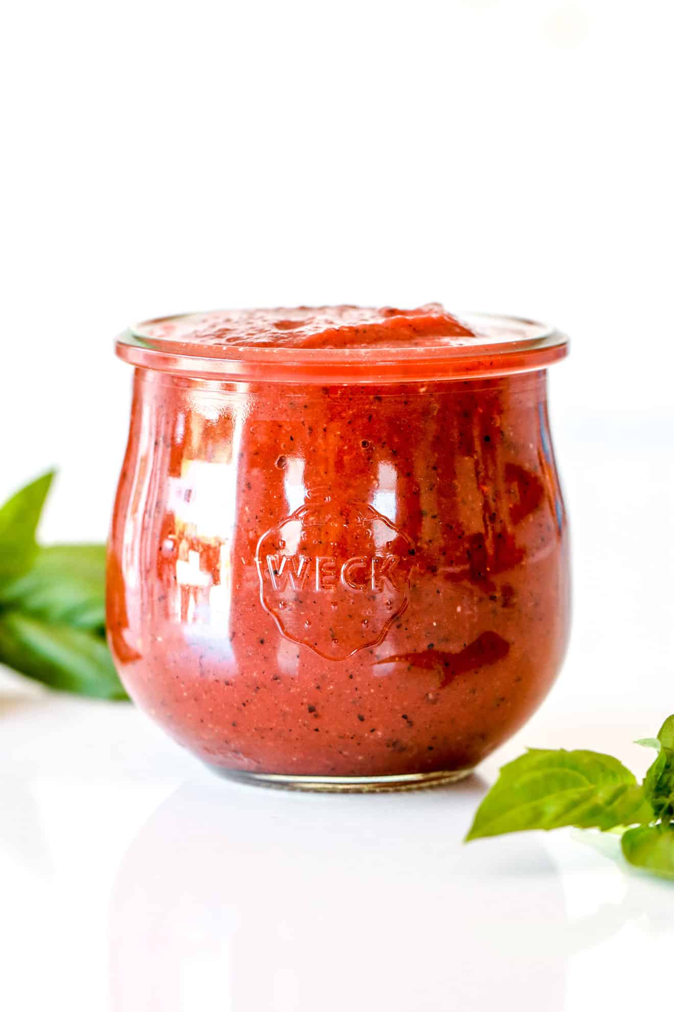 weck jar filled with homemade pizza sauce on white counter with basil leaves