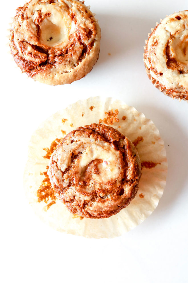 overhead image of three pumpkin cream cheese swirl muffins one with its muffin wrapper unwrapped sitting on a white counter