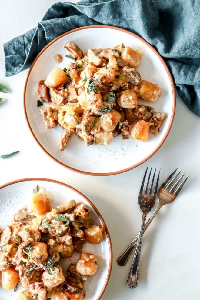 overhead image of two white plates with cauliflower gnocchi in a creamy sauce with caramelized onions, sausage, and chopped sage