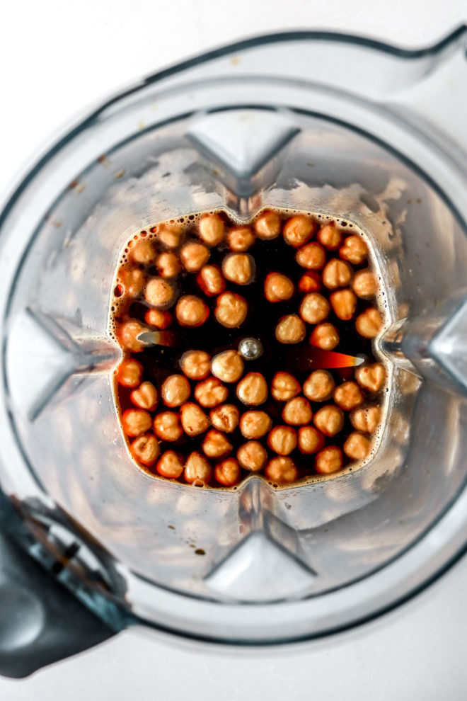 overhead image of a blender with coffee and hazelnuts in it on a white counter