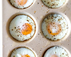 overhead image of half of a muffin tin with six oven-baked eggs sprinkled with pepper