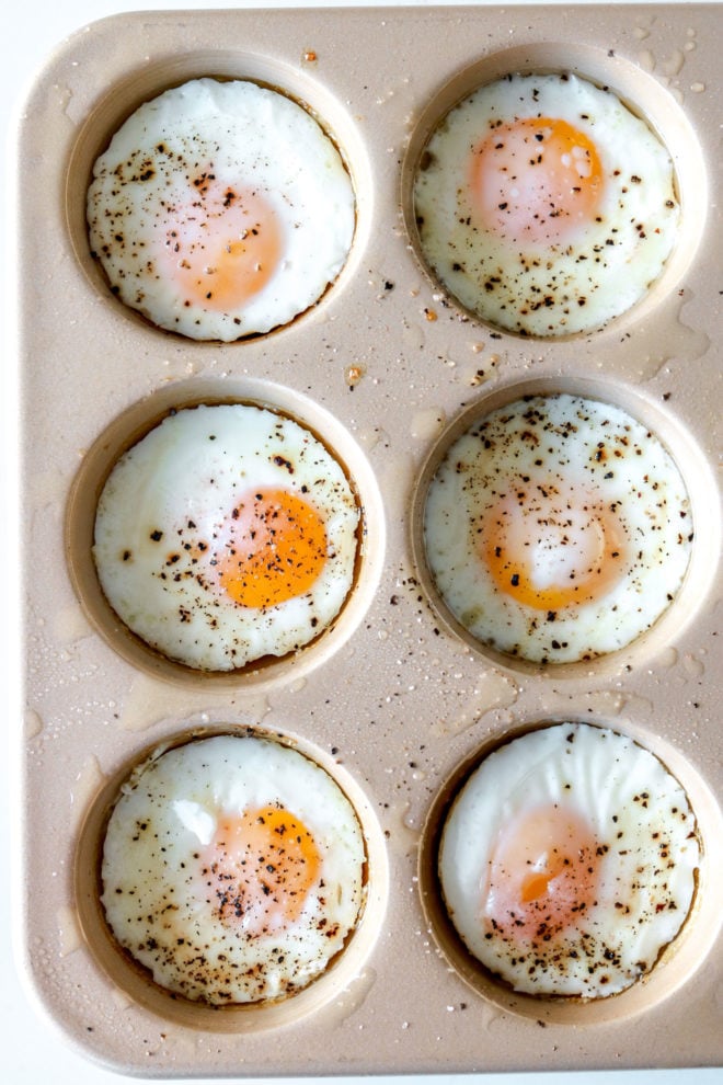 overhead image of half of a muffin tin with six baked eggs sprinkled with pepper