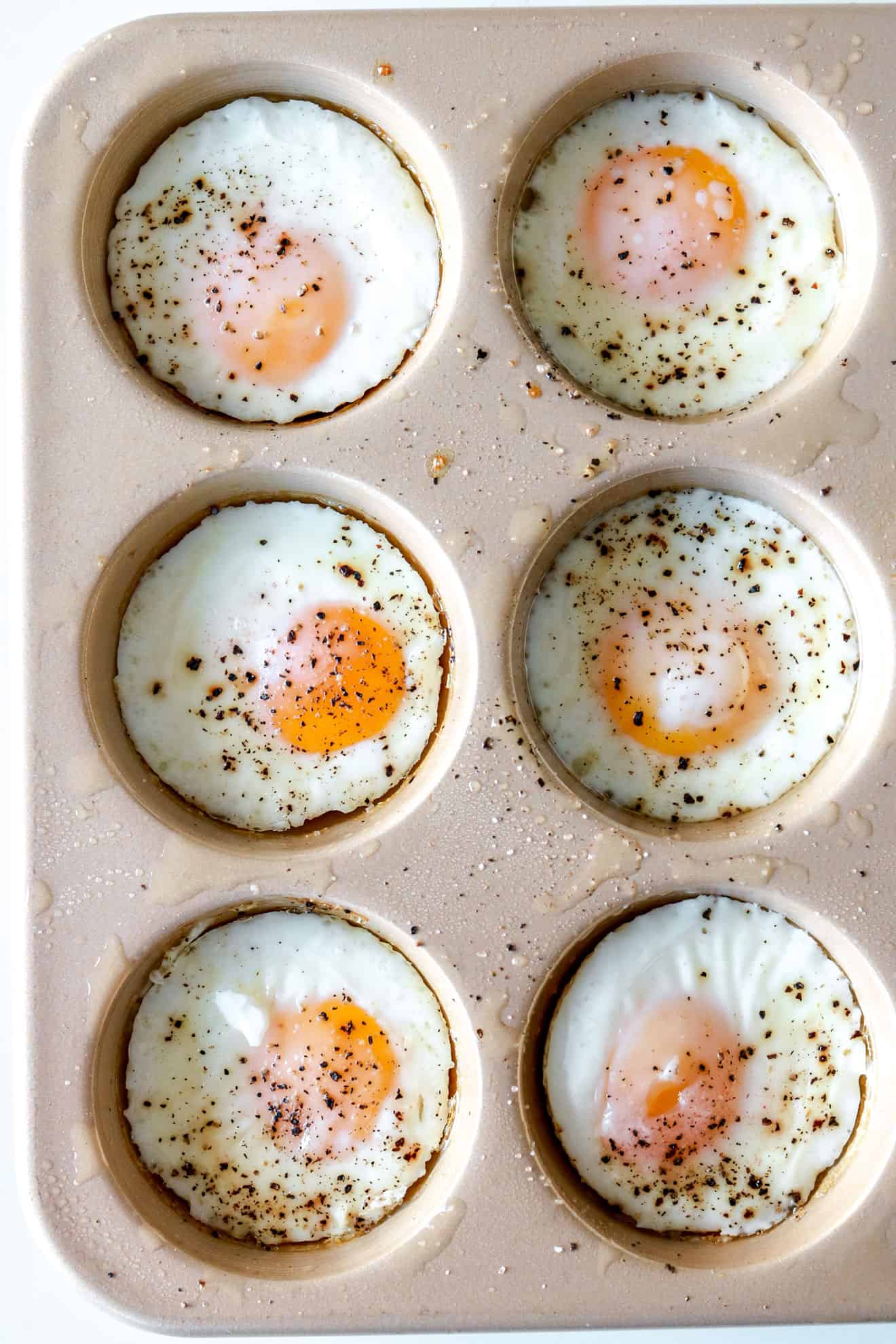 overhead image of half of a muffin tin with six oven-baked eggs sprinkled with pepper