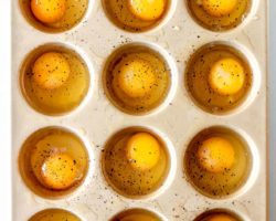 overhead image of a muffin tin filled with 12 raw eggs sprinkled with pepper
