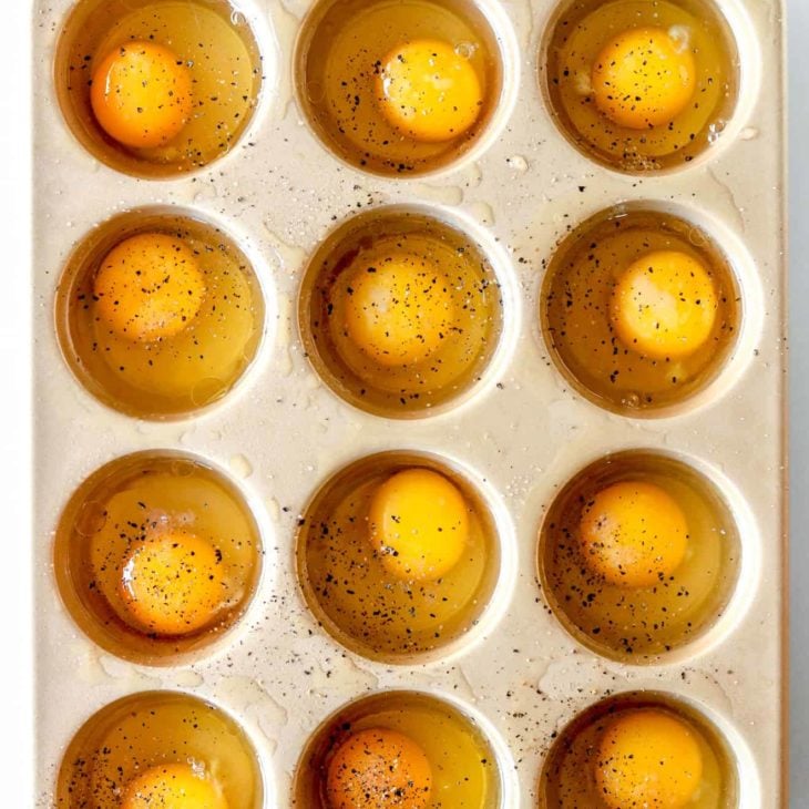 overhead image of a muffin tin filled with 12 raw eggs sprinkled with pepper