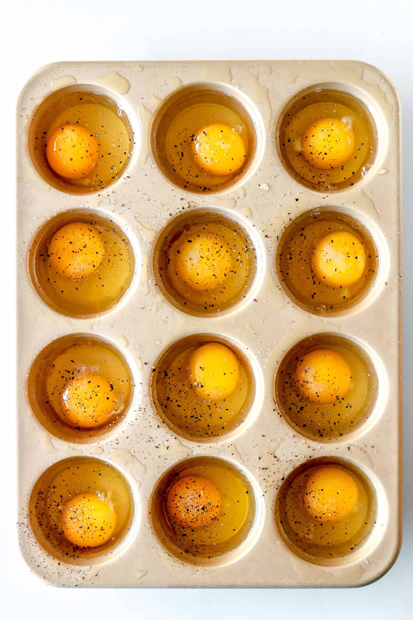 overhead image of a muffin tin filled with 12 raw eggs sprinkled with pepper