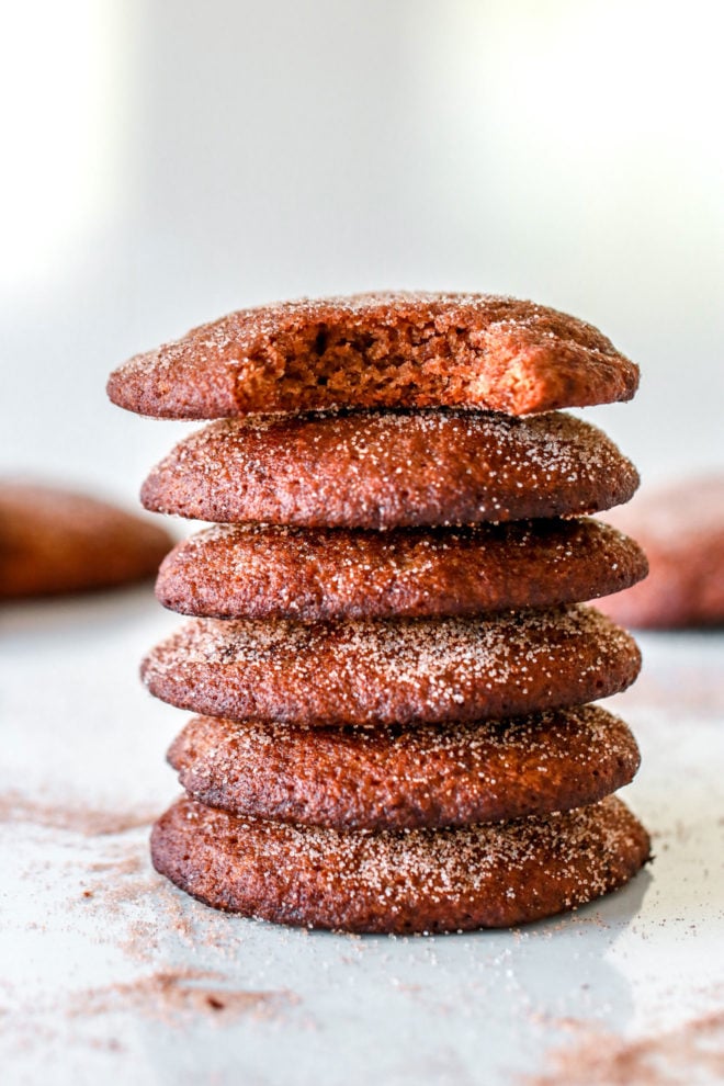 side image of a stack of snickerdoodles on a white counter, the top cookie has a bite taken out