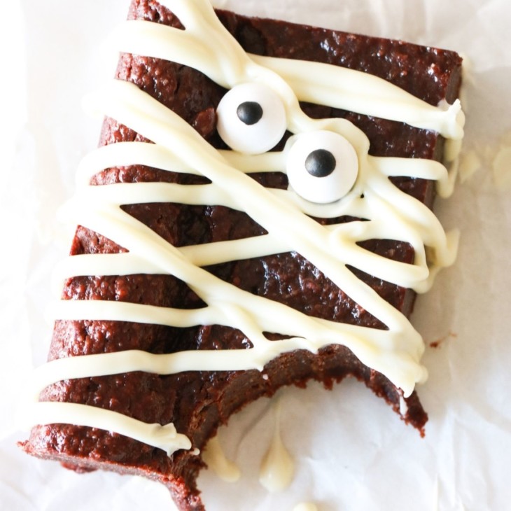 fudgey gluten free mummy brownie with white chocolate drizzled and candy eyeballs with a bite taken out