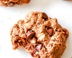 overhead view of a cookie with chocolate chips, oats, and a bite taken out laying on a white counter