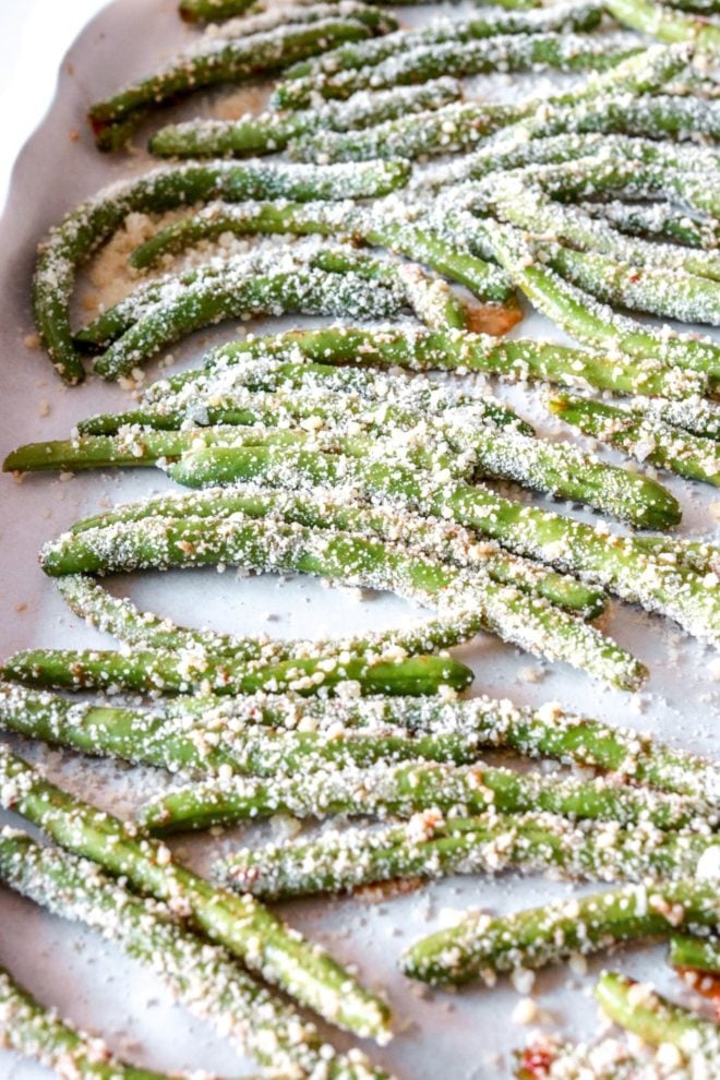side view of raw green beans coated with parmesan cheese on baking sheet lined with parchment paper