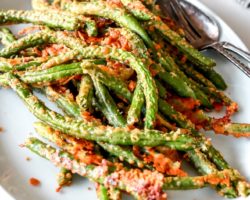 side view of parmesan crusted green beans on white plate on white counter