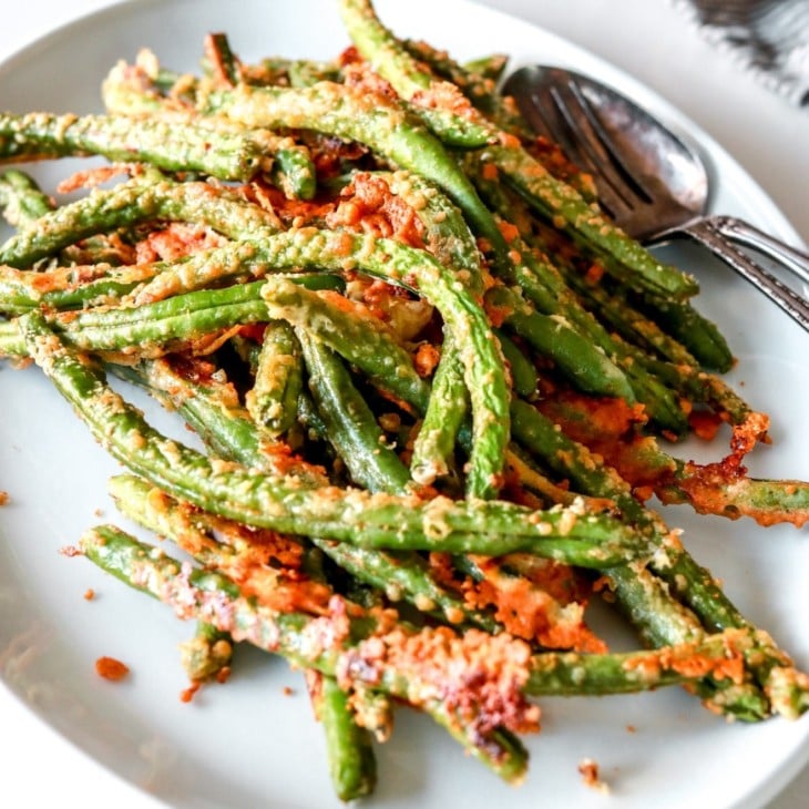 side view of parmesan crusted green beans on white plate on white counter