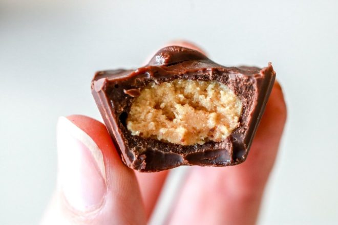 fingers holding a chocolate peanut butter cup with a bite taken out