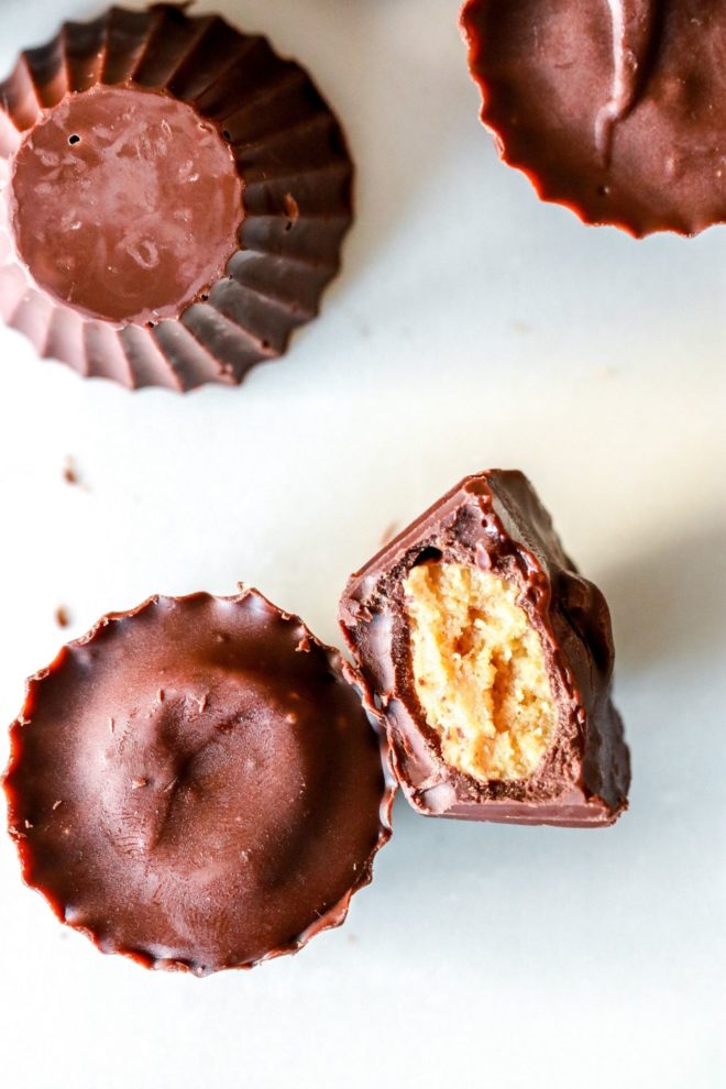 overhead image of chocolate peanut butter cups on a white counter, one with a bite taken out