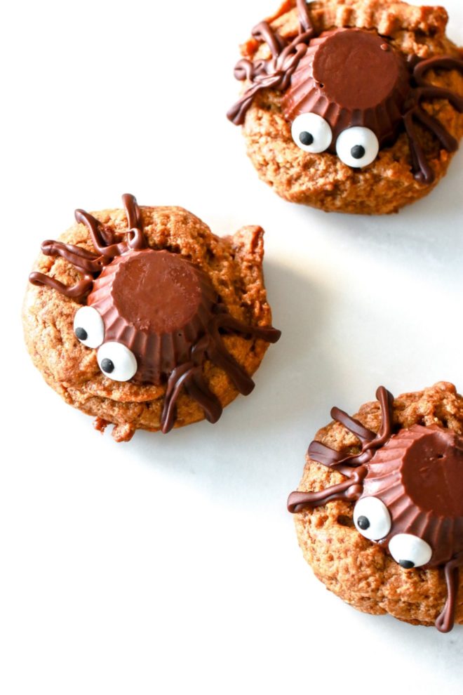 overhead image of peanut butter cookies with an upside down chocolate peanut butter cup, chocolate lines, and candy eyeballs to decorate the cookie as a spider