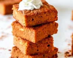 stack of pumpkin bars on white counter, the top bar on the stack has a dollop of whipped cream