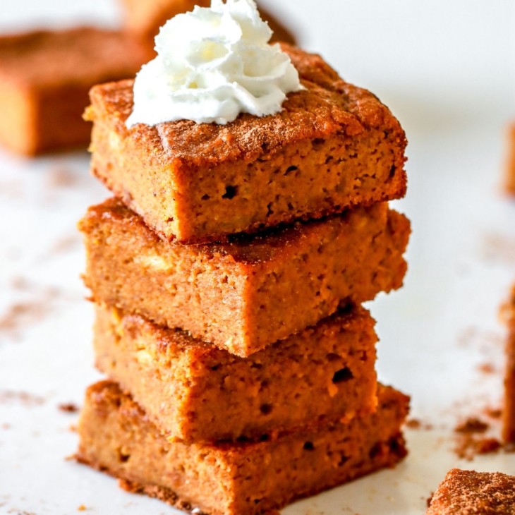 stack of pumpkin bars on white counter, the top bar on the stack has a dollop of whipped cream