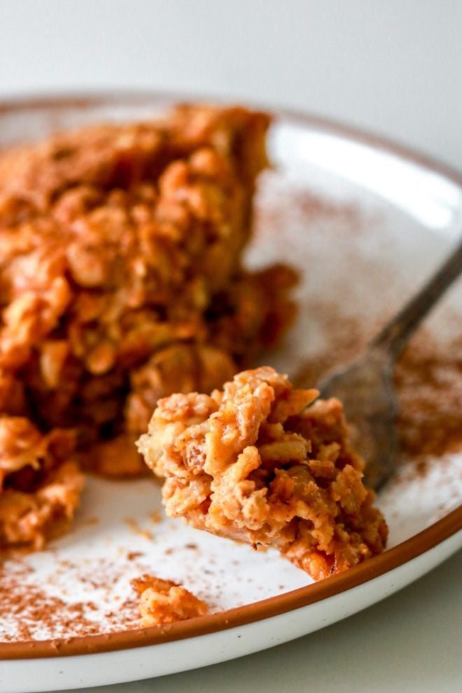 close up image of a fork with a bite of baked pumpkin oatmeal leaning on the edge of a white plate