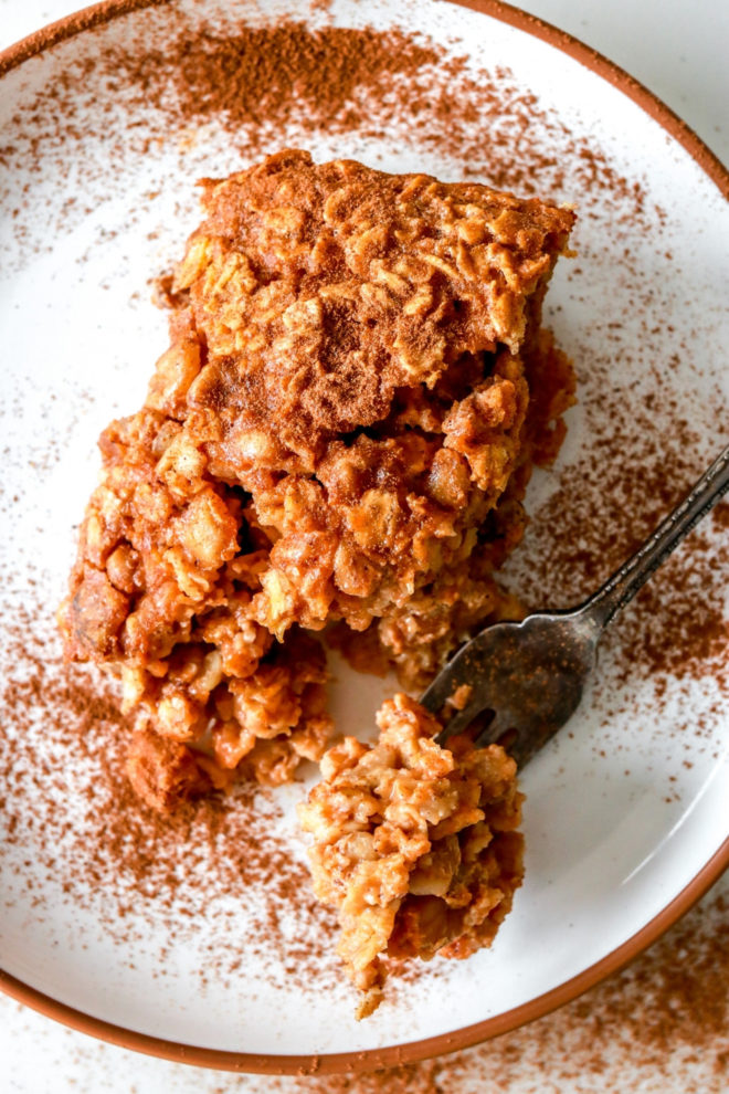 overhead image of a white plate with a slice of baked oatmeal with spice sprinkled on top and a fork taking off a bite