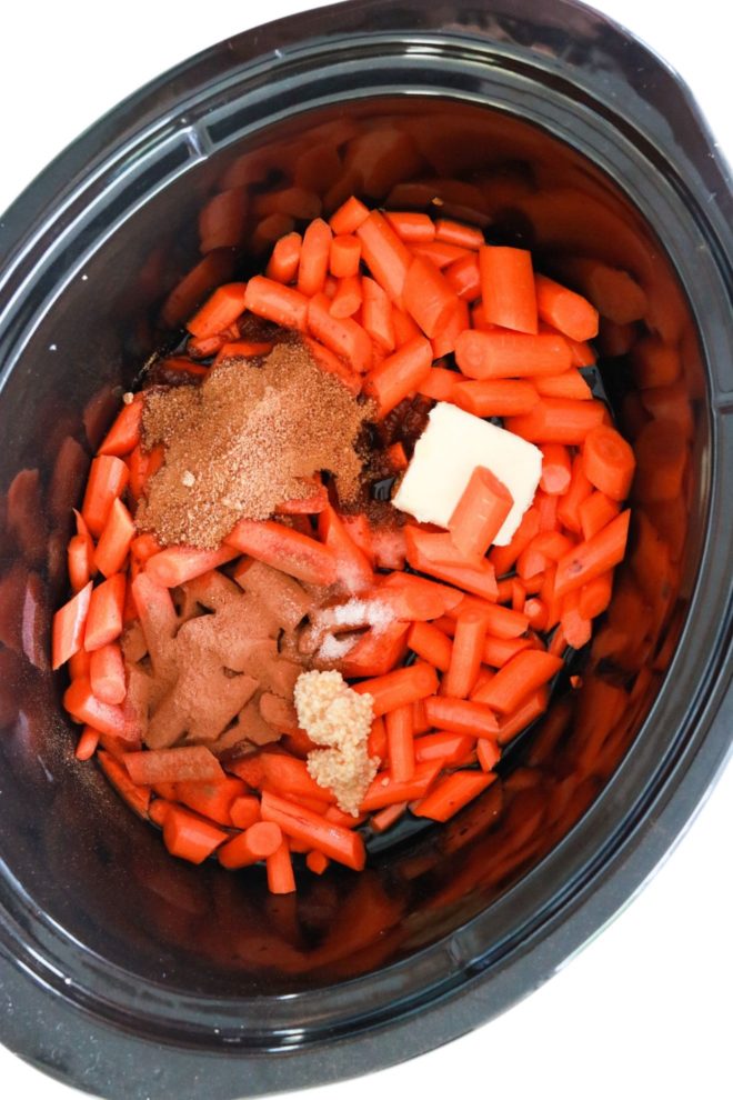 slow cooker crockpot with chopped carrots, sugar, butter, minced garlic, and spices inside it