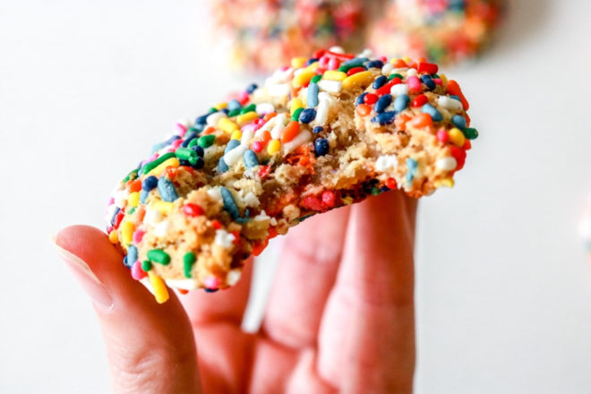 hand holding a sprinkle cookie with a bite taken out