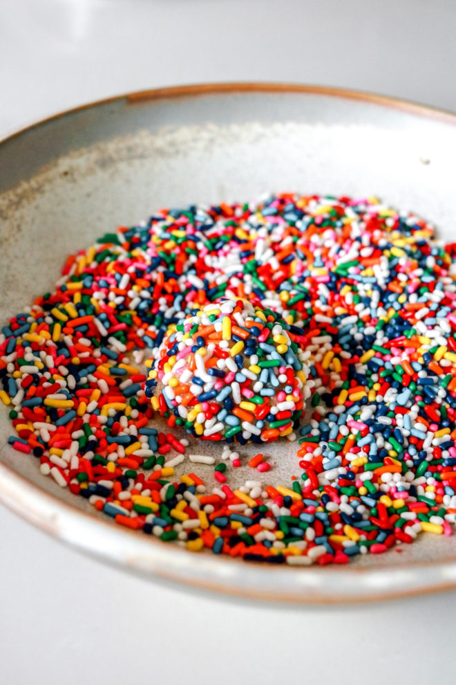 side view of a shallow bowl with sprinkles and a raw cookie dough ball rolled in sprinkles