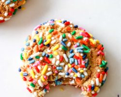overhead image of a gluten free sprinkle cookie with a bite taken out on a white counter