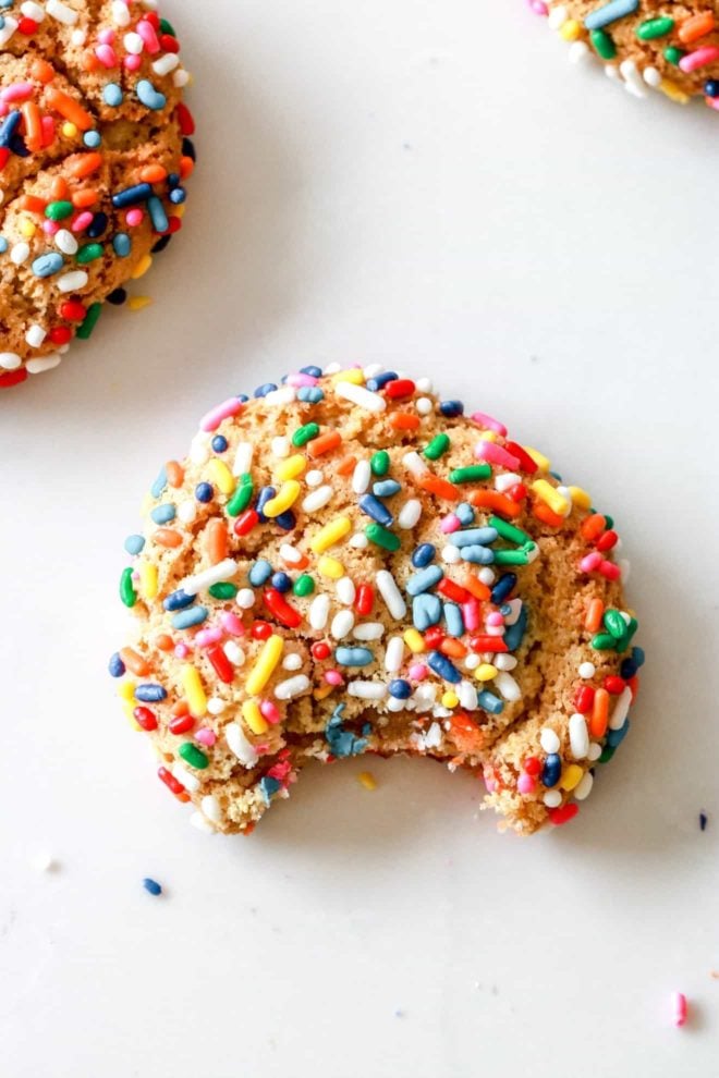 overhead image of a gluten free sprinkle cookie with a bite taken out on a white counter