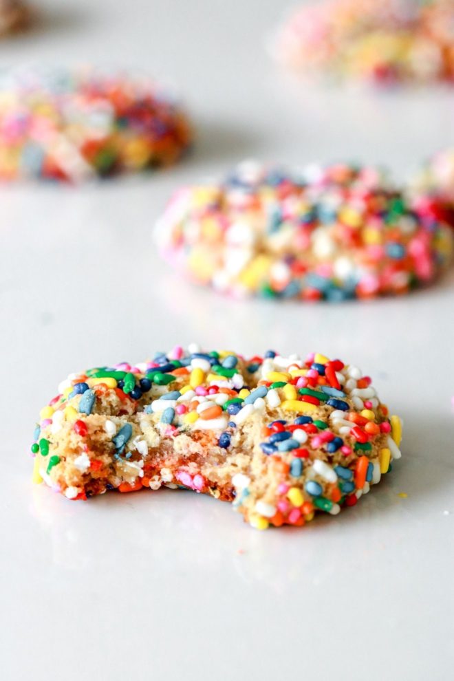 side view of a sprinkle cookie with a bite taken out on a white counter with other cookies blurred in the background