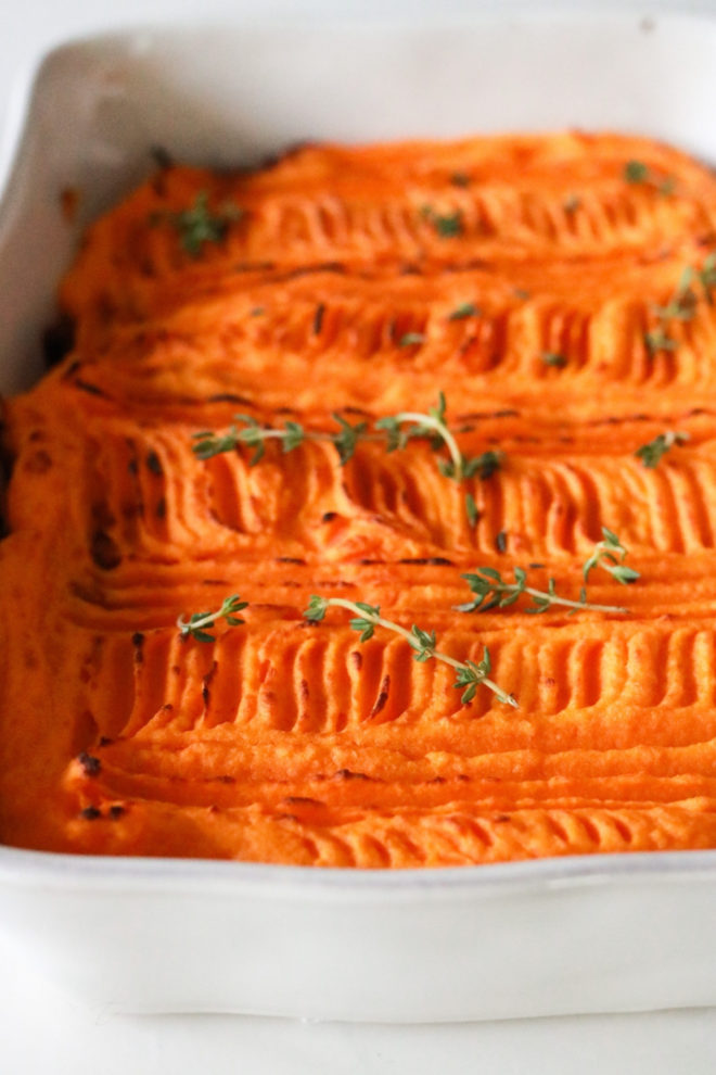 side view of a white baking dish with sweet potato puree and thyme leaves