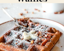 side view of a waffle with butter on a white plate and powdered sugar is being sprinkled onto the waffle