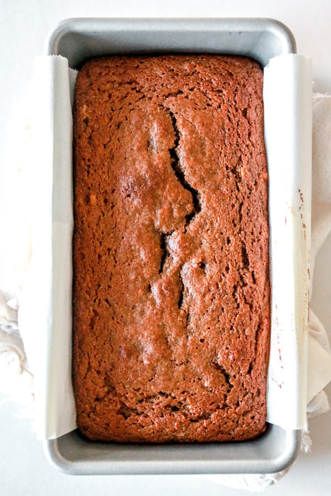 overhead image of a loaf pan with parchment paper and a baked banana gingerbread