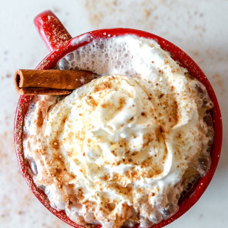 overhead image of a warm beverage with whipped cream, a cinnamon stick, and spice sprinkled on top
