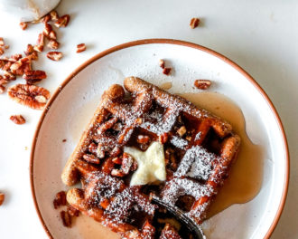 overhead image of white plates with waffles on them. waffles are topped with butter, syrup, pecans, and powdered sugar.