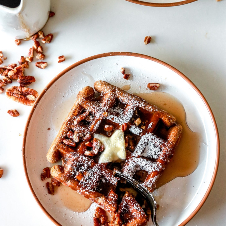 overhead image of white plates with waffles on them. waffles are topped with butter, syrup, pecans, and powdered sugar.