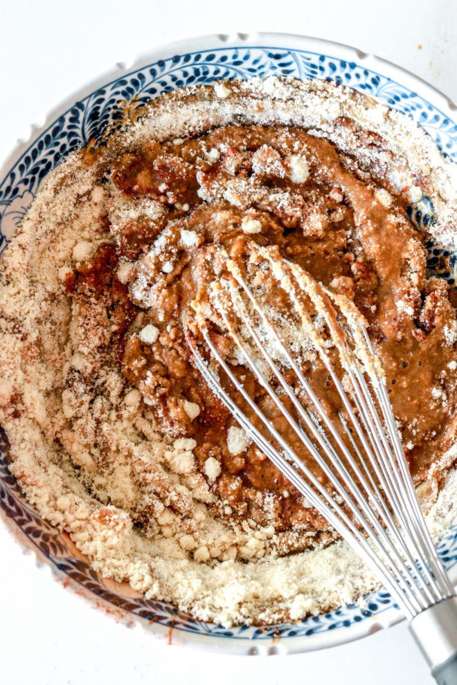 overhead image of a white and blue bowl with half mixed gingerbread waffle batter and a whisk in it