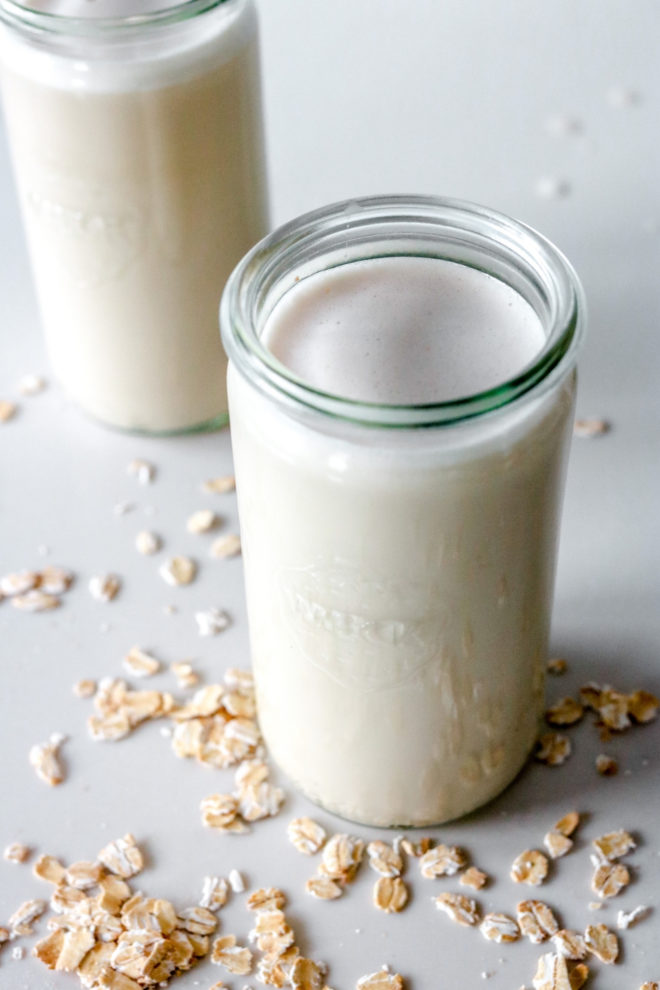 weck jar filled with oat milk on a white counter with oats scattered around it