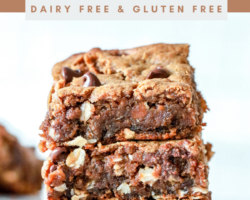 side view of a stack of three oatmeal peanut butter cookie bars loaded with oats, chocolate chips, and peanuts. the stack sits on a white counter with crumbs and other cookie bars blurred in the background. text overlay reads "oatmeal peanut butter cookie bars dairy free & gluten free"