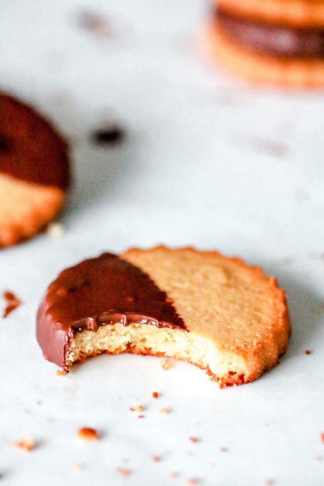 side view of a circle shortbread cookie half dipped in chocolate with a bite taken out