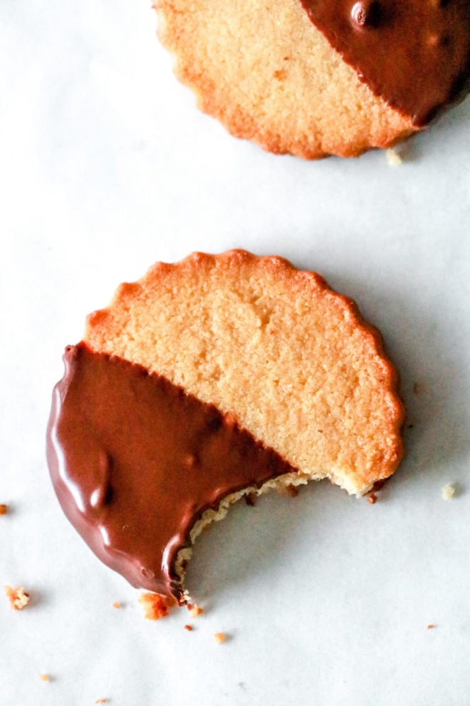 overhead image of a circle shortbread cookie half dipped in chocolate with a bite taken out