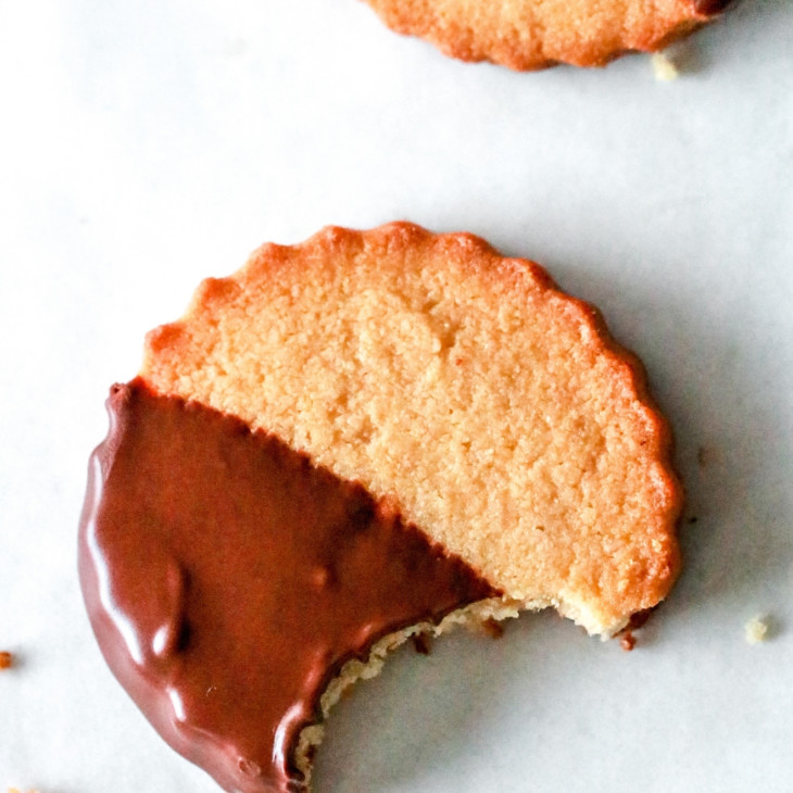 overhead image of a circle shortbread cookie half dipped in chocolate with a bite taken out