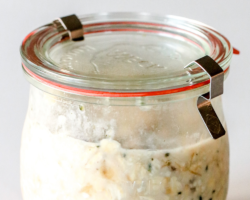 This image is a side view of a weck jar with oatmeal inside. The jar has a lid on it and sits on a white counter. Text overlay reads "banana overnight oats."