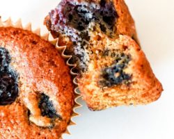 This is an overhead image of a blueberry muffin with a bite taken out of it. The muffin lays on it side, leaning up against another muffin on a white counter.